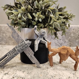 May include: Three small 3D printed figurines. One is a grey, angular, geometric dragonfly-like shape. Another is a grey, textured, humanoid figure in a seated pose. The third is a solid, light brown, multi-limbed creature with a smooth finish.