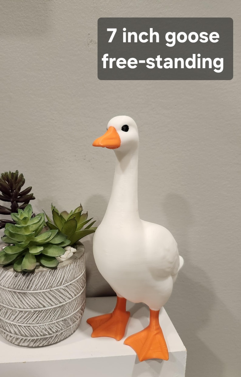 May include: A white goose figurine with an orange beak and orange webbed feet. The goose is free-standing and measures 7 inches in height as indicated by the text overlay. The figure has a smooth matte finish and black eyes.