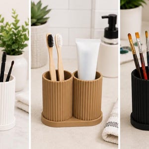 May include: A set of three double-cylinder organisers with a vertical ribbed texture, available in white, tan, and black. Each organiser features two connected cylindrical compartments on a shared oval base, suitable for holding brushes, pens, or toiletries.