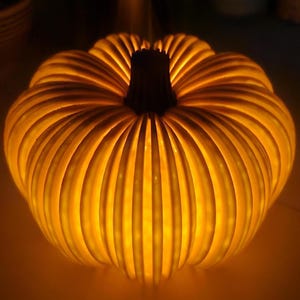 May include: A glowing, illuminated pumpkin-shaped decoration. The pumpkin has a ribbed design with a dark brown stem. The warm light emanates from within, creating a festive and inviting ambiance. Perfect for fall and Halloween decor.