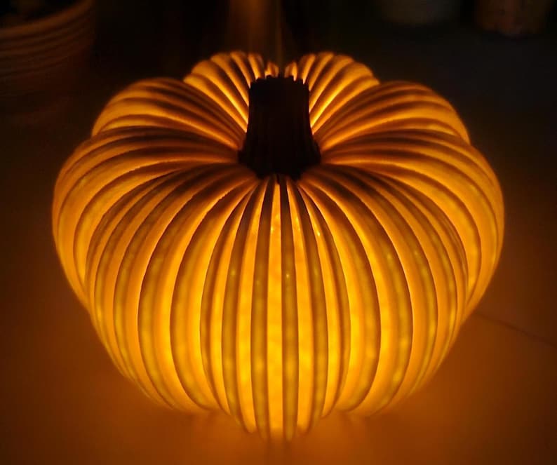 May include: A glowing, illuminated pumpkin-shaped decoration. The pumpkin has a ribbed design with a dark brown stem. The warm light emanates from within, creating a festive and inviting ambiance. Perfect for fall and Halloween decor.