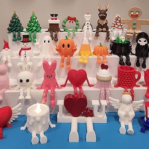 May include: A collection of 3D printed shelf-sitting figurines featuring various seasonal characters including Christmas trees, a snowman, a ghost, pumpkins, a gingerbread person, hearts, a cupcake, a mug, a rose, an angel, and a patriotic top hat.