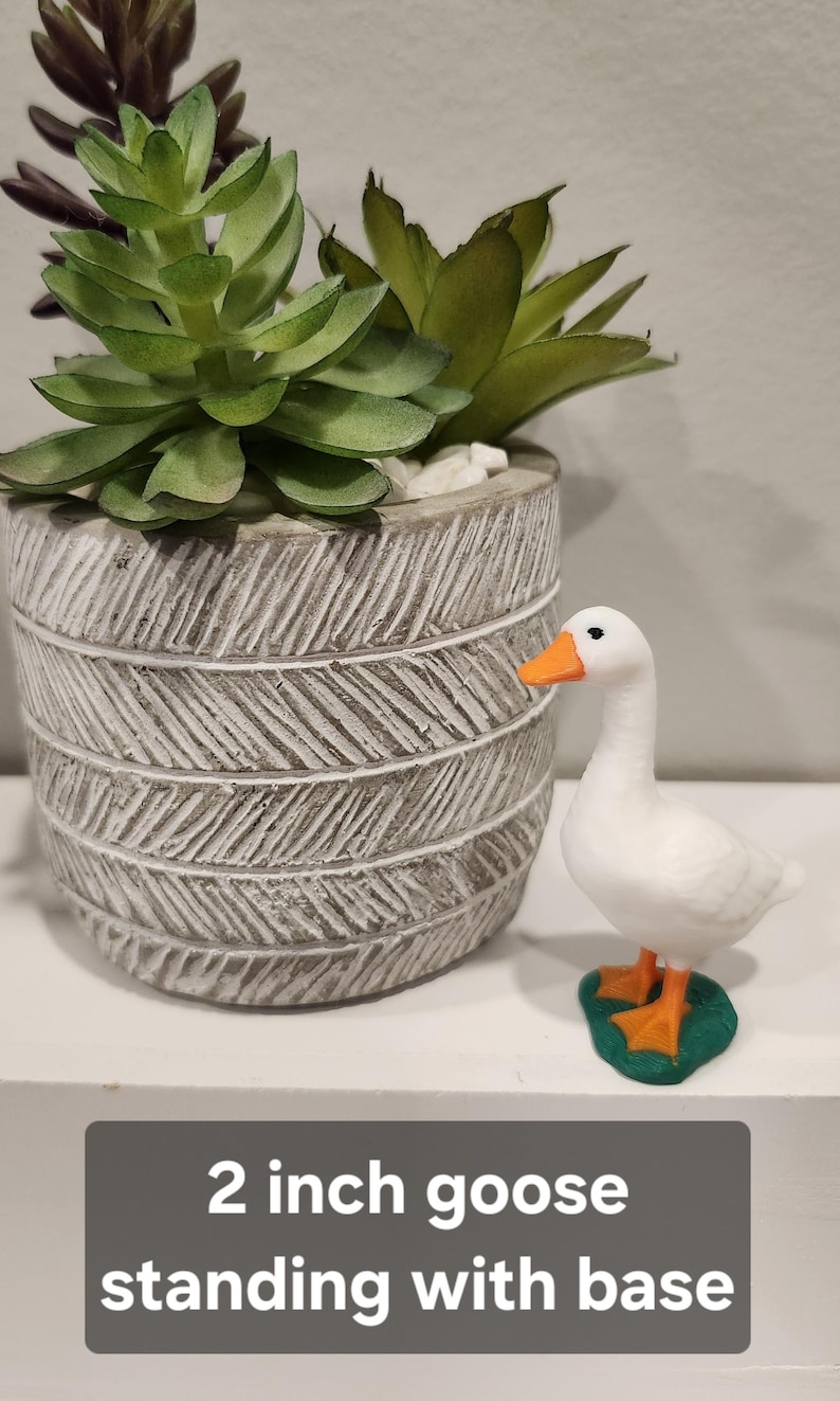 May include: A white goose figurine with an orange beak and feet, standing on a green base, labeled 2 inch goose standing with base. Next to it is a gray cylindrical planter with a textured herringbone pattern containing green succulents.