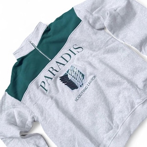 Può includere: Felpa grigia con un pannello verde sulle spalle e sulla parte superiore del petto. La parola "PARADIS" è stampata in verde sopra uno stemma con le parole "SCOUTING LEGION" sotto. La felpa ha una chiusura con zip.