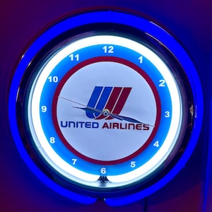 May include: A circular wall clock with a blue neon light surround. The clock face displays the United Airlines logo in red and blue, with the text "UNITED AIRLINES". The clock has black hands and white numerals.