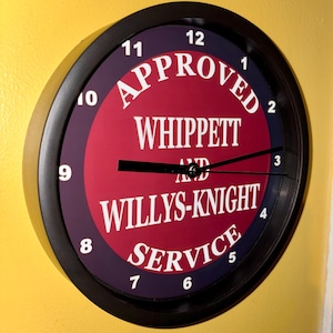 May include: A circular wall clock with a black surround. The clock face is red and purple with white text reading "APPROVED WHIPPETT AND WILLYS-KNIGHT SERVICE". The clock hands are black.