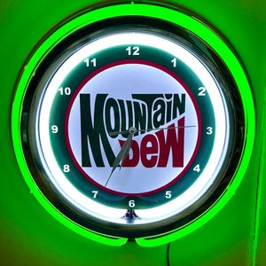 May include: A neon green and white Mountain Dew clock. The clock face features the Mountain Dew logo in green and red. The clock is round with a green neon border and a black power cord.