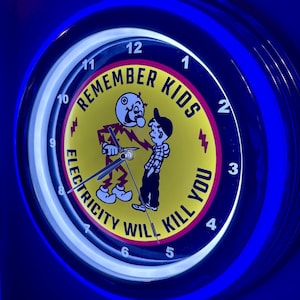 May include: A round neon clock with a blue outer ring and a yellow center. The clock face features a cartoon illustration with the text "REMEMBER KIDS ELECTRICITY WILL KILL YOU". The clock hands point to 10:08.