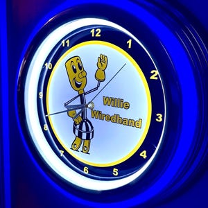 May include: A circular, illuminated clock with a blue surround and a white face. The clock face displays the text "Willie Wiredhand" and a cartoon character. The numbers are in a yellow font.