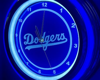 May include: A blue neon clock with the word "Dodgers" in white script. The clock face has white numerals and hands, and is surrounded by a blue neon light. The clock is a sports-themed item.