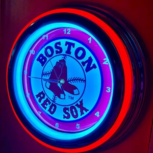 May include: A neon clock with a red and blue illuminated border. The clock face is blue with the words "BOSTON RED SOX" in white and the team logo. The clock has a black frame.