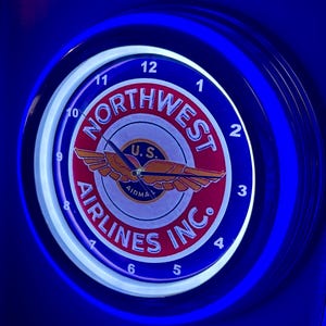 May include: A circular, illuminated clock with a blue and white border. The clock face displays "NORTHWEST AIRLINES INC." in a red and white design, with an aeroplane logo. Numbers 1-12 are visible around the clock face.