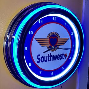 May include: A circular wall clock with a blue neon light. The clock face is white with the Southwest Airlines logo and the word "Southwest". The clock has black hands and red numbers.
