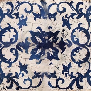 May include: Rectangular tile with a distressed, crackled white background and a repeating pattern of dark blue floral and scroll designs. The design is symmetrical, with a central floral motif.