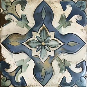 May include: Square ceramic tile with a detailed floral and geometric design. The tile features a central flower motif surrounded by stylized leaves and curved shapes in shades of blue, green, and white. The edges have a distressed, aged appearance.