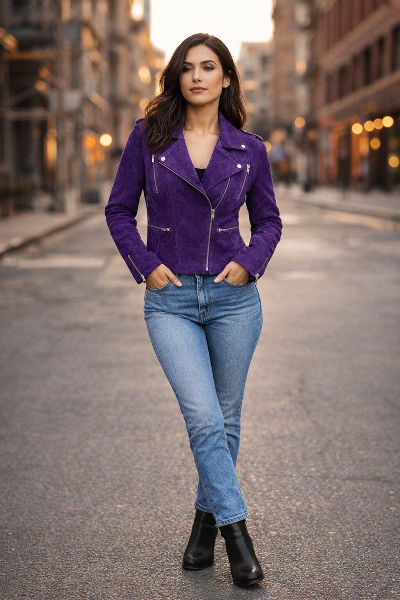 May include: A person wearing a purple suede jacket with silver zips, light blue jeans, and black ankle boots. The jacket has a classic biker style. The background is a city street.