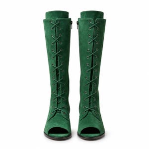 May include: A pair of knee-high boots in a vibrant green suede material. These boots feature an open-toe design and a full-length front lace-up closure with dark metal eyelets and matching green laces. The boots have a structured shaft and a flat sole.