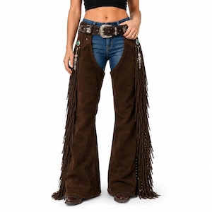 May include: Dark brown suede leather chaps featuring long fringe along the outer legs, silver-toned metal conchos with turquoise accents, and a matching brown leather belt with an ornate silver buckle worn over blue denim jeans.