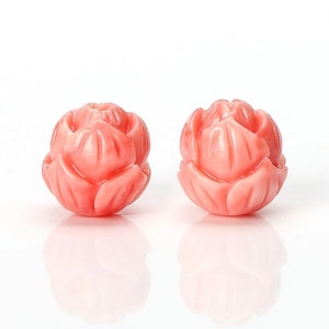 May include: Two pink coral flower beads with intricate carvings. The beads are round and have a three-dimensional flower design.