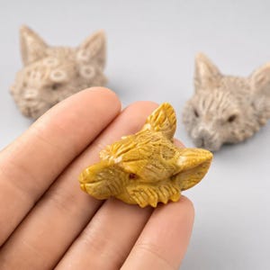 以下が含まれることがあります： 手彫りの石で作られた動物の頭の小さな置物が3つ。1つはマスタードイエローの石で小さな赤い目のディテールがあり、他の2つはライトベージュの石で毛並みの質感が彫り込まれています。それぞれ尖った耳と鼻先が特徴です。