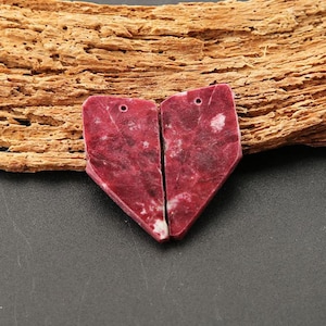 Peut inclure: Deux pendentifs assortis en forme de cœur, taillés dans une pierre magenta foncé et rouge sombre avec des marbrures blanches naturelles. Chaque pièce présente un petit trou circulaire au sommet pour la suspension, avec une surface polie.