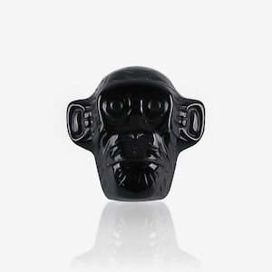 May include: A glossy black sculpture of a chimpanzee's head. The sculpture has detailed facial features, including eyes, ears, and a mouth. The sculpture is set against a white background.