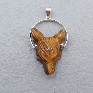 Peut inclure: Un pendentif en argent avec une tête de loup en œil de tigre sculptée. Le pendentif est sur une chaîne en argent avec un anneau rond.