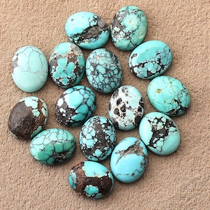 May include: A collection of fourteen oval-shaped turquoise cabochons, each featuring a unique pattern of light blue and teal hues with dark brown or black matrix veining. The stones vary in size and display smooth, polished, rounded surfaces.