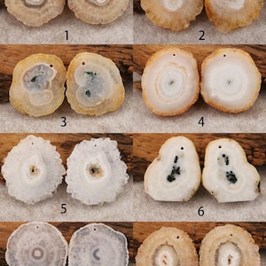 May include: A collection of eight pairs of polished agate slices, each with a unique pattern of concentric rings and a central cavity. The colors range from creamy white and beige to shades of brown and orange. Each slice has a small drilled hole.