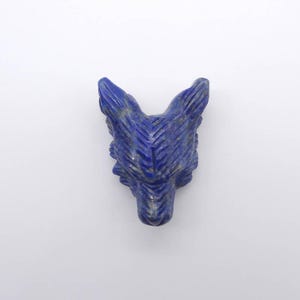 May include: A carved lapis lazuli wolf head sculpture. The sculpture is a deep blue color with gold flecks, and the details of the wolf's face are clearly defined. The sculpture is a unique decorative item.