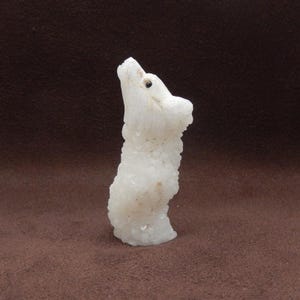 Peut inclure: Une sculpture en cristal blanc représentant un ours, avec un œil noir. L'ours est debout, la tête inclinée vers le haut. La sculpture a une surface rugueuse et texturée, sur fond marron.