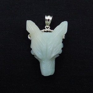 May include: A white wolf pendant carved from a light green stone. The pendant is attached to a silver chain.