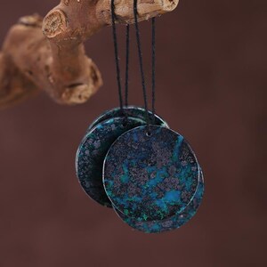 Puede incluir: Tres piedras decorativas redondas y planas con un patrón moteado turquesa y negro, suspendidas por cuerdas negras de una rama de madera. Las piedras tienen un aspecto texturizado, con una mezcla de colores turquesa y gris oscuro.