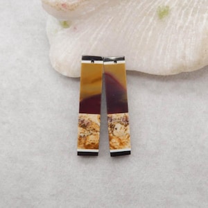 May include: Two rectangular, natural stone pendants. Each pendant features a mix of colors, including tan, burgundy, and cream, with black and white accents. The pendants are likely for jewelry making or crafting.