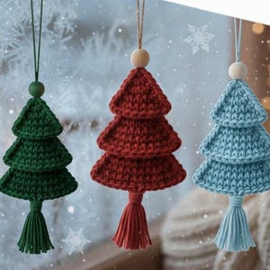 May include: Three crocheted Christmas tree ornaments in green, red, and blue. Each tree has a tassel at the bottom and a wooden bead at the top, suspended by a string. The background features snowflakes and soft lighting.