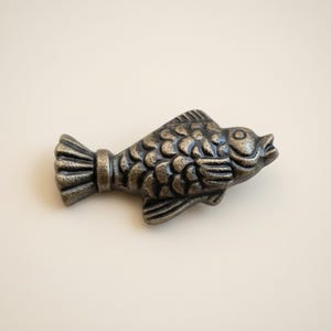 May include: A bronze-colored fish-shaped decorative object. The fish has detailed scales, fins, and a tail. The object is likely made of metal and is designed to be a decorative element.