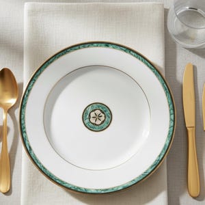May include: White dinner plate with a green and gold decorative border. The plate has a gold rim and a central design with a star-like pattern. A gold spoon and knife are visible.