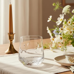 May include: A clear glass tumbler featuring a subtle, embossed pattern of small, rounded indentations around the exterior. The glass has a smooth, curved silhouette and a thick, weighted base, providing a stable and balanced structure for daily use.