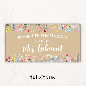 Op de afbeelding: Een rechthoekig bord met een beige achtergrond, versierd met bloemstukken aan de boven- en onderkant. De tekst luidt "FRESH OFF THE MARKET, THE FUTURE Mrs. Belmont" in witte letters. Het Lulie Lane-logo staat onderaan.