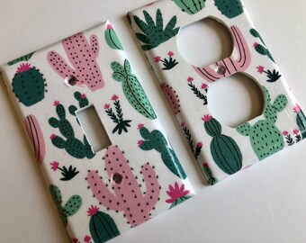 Peut inclure: Deux caches de prise et d'interrupteur blancs avec un motif de cactus. Le motif présente des cactus roses et verts sur un fond blanc.