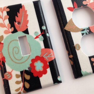 May include: Two decorative light switch covers. One has a single switch opening, the other has two outlet openings. Both feature a black and white striped background with floral designs in coral, teal, and gold.