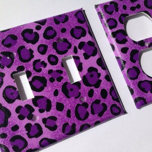 May include: Two purple and black leopard print light switch and outlet covers. The switch cover has two toggle switches and the outlet cover has two standard outlets.
