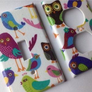 May include: Two decorative wall plates featuring a colorful bird and owl pattern. The plates are designed to cover electrical outlets and light switches.