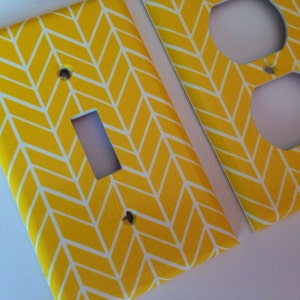 May include: Two yellow and white patterned light switch and outlet covers. The pattern is a herringbone design with white lines on a yellow background.