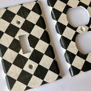 May include: Two decorative wall plates with a black and white checkered pattern. One plate has a single light switch opening and the other has a double outlet opening.