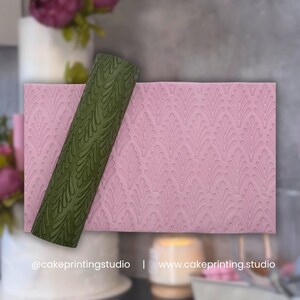 May include: A pink cake decorating mat with a repeating leaf pattern. A green rolling pin with a matching leaf design is placed on the mat. The text "@cakeprintingstudio | www.cakeprinting.studio" is visible.