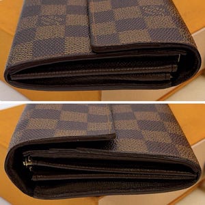 May include: Close-up of a brown and tan checkered pattern wallet. The wallet has a dark brown border and a flap closure. The interior of the wallet is visible, showing multiple compartments for cards and cash.