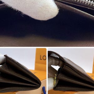 May include: Close-up of a brown leather wallet, partially open, revealing interior compartments. The wallet has a zipper closure and a gold-colored zipper pull. The leather appears to have a textured finish.