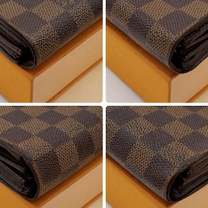 May include: Close-up of a brown and tan checkered wallet. The wallet is resting on a tan box. The wallet has a repeating pattern of squares.