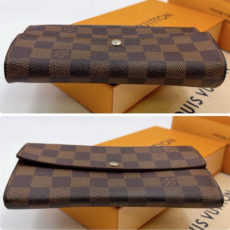 May include: A brown and tan checkered pattern wallet with a snap closure. The wallet is rectangular and has a flap that folds over to close. The wallet is sitting on top of a box.